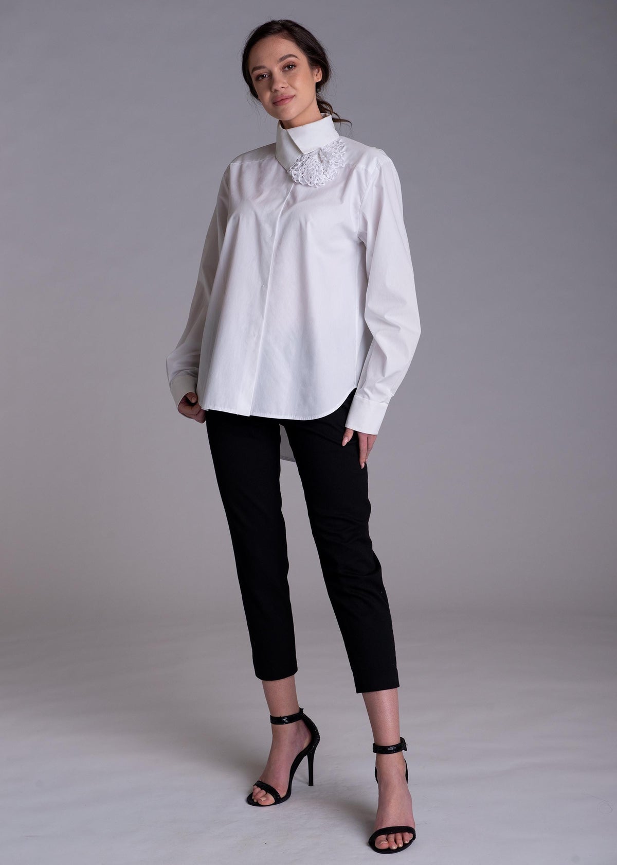 May include: A white long-sleeved button-down shirt with a high collar and a textured white floral appliqué detail on the right side, paired with slim-fit black trousers and black high-heeled sandals with ankle straps.