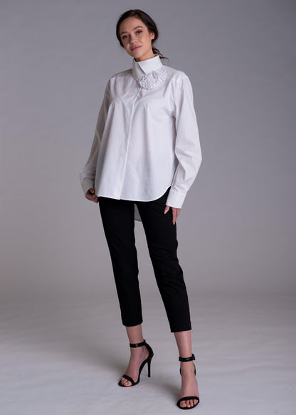 May include: A white long-sleeved button-down shirt with a high collar and a textured white floral appliqué detail on the right side, paired with slim-fit black trousers and black high-heeled sandals with ankle straps.