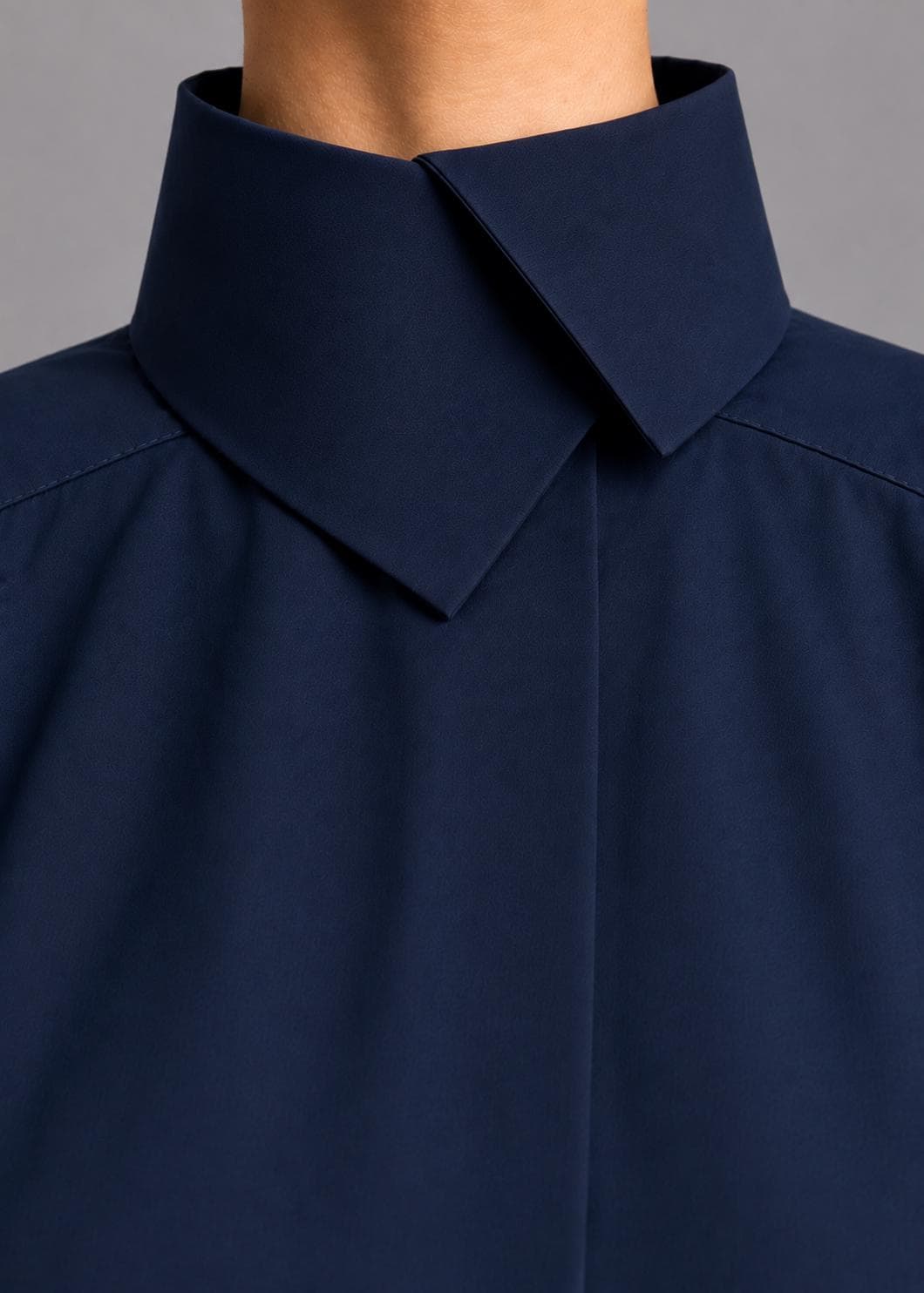 May include: A dark navy blue shirt featuring a high, structured stand-up collar with a pointed, overlapping front closure. The garment is crafted from a smooth, solid-colored fabric with clean, minimalist lines and visible shoulder seam stitching.