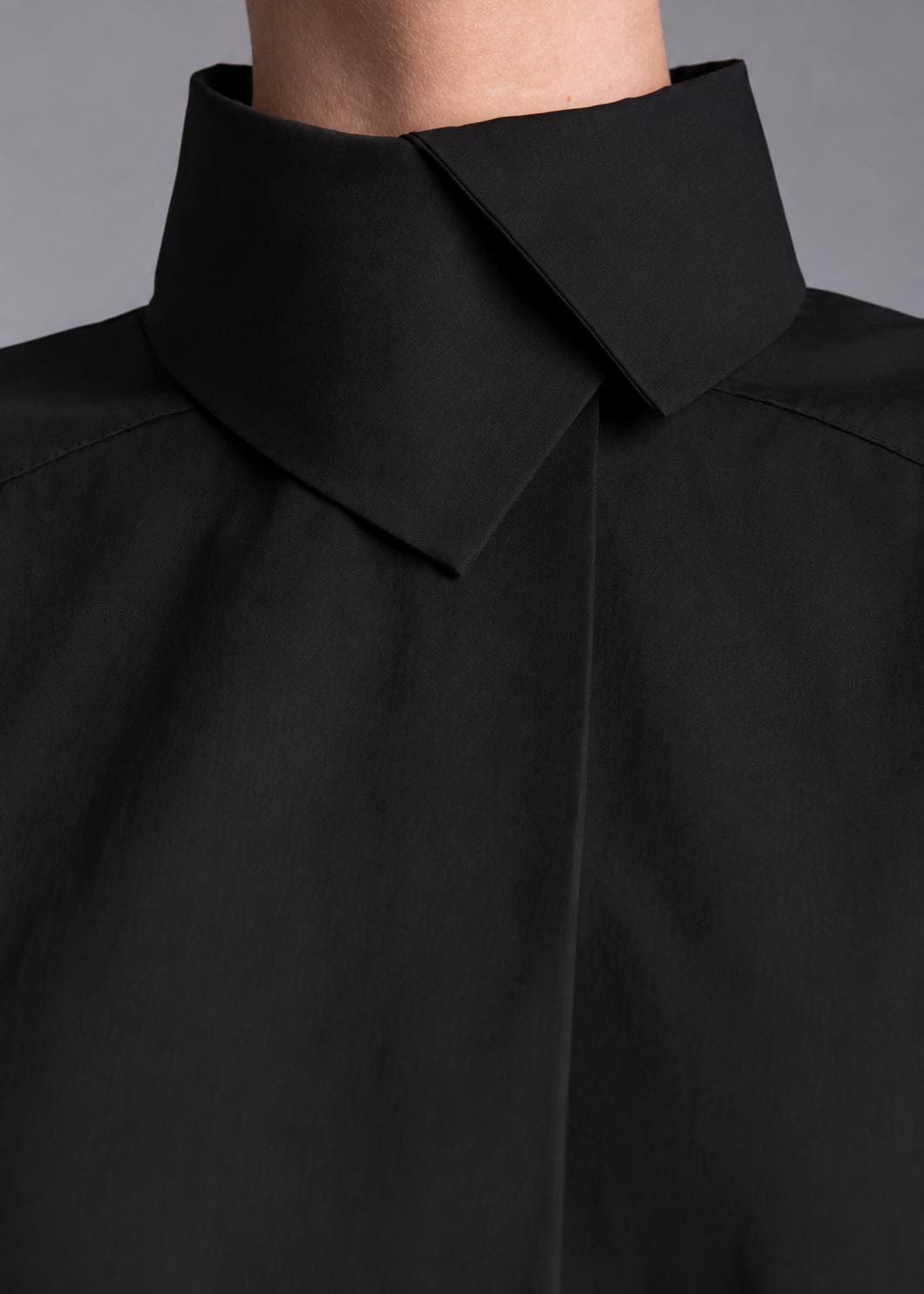 May include: A solid black shirt featuring a high, structured collar with a sharp, pointed fold that overlaps at the front. The garment is crafted from a smooth, matte fabric and displays clean, minimalist lines around the neck and shoulder area.