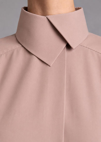 May include: A dusty rose shirt featuring a high, structured collar with a pointed, overlapping design. The garment has a smooth, matte finish and a clean, minimalist front placket that conceals the buttons, creating a seamless appearance.
