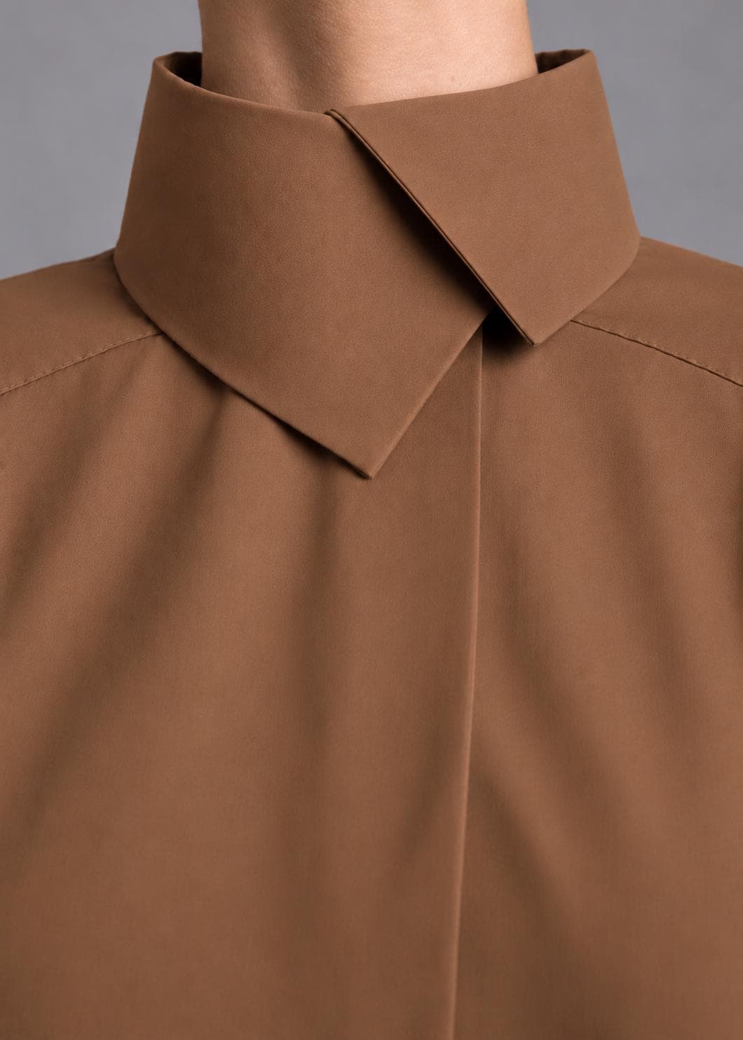 May include: A solid brown shirt featuring a high, structured collar with a sharp, overlapping point design. The garment has a smooth, matte texture and clean, minimalist lines, with visible stitching along the shoulder seams and a concealed placket.