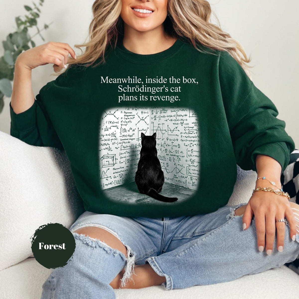 May include: A dark forest green crewneck sweatshirt featuring a graphic of a black cat sitting in front of a wall covered in complex physics equations. The text above the graphic reads, "Meanwhile, inside the box, Schrödinger's cat plans its revenge."