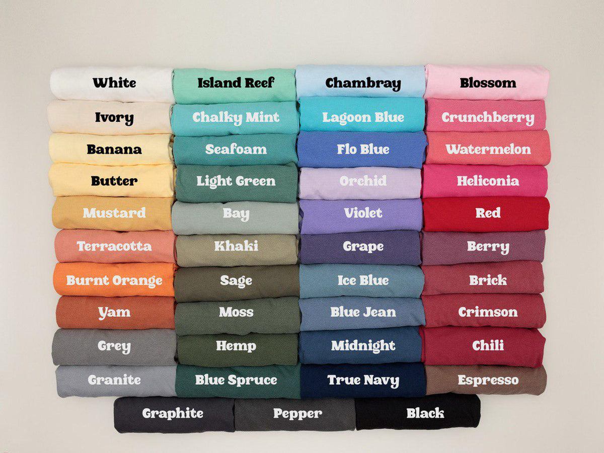 May include: A collection of folded t-shirts arranged in a grid, showcasing a wide variety of colors including white, ivory, banana, butter, mustard, terracotta, burnt orange, yam, grey, granite, island reef, chalky mint, seafoam, light green, bay, khaki, sage, moss, hemp, blue spruce, chambray, lagoon blue, flo blue, orchid, violet, grape, ice blue, blue jean, midnight, true navy, blossom, crunchberry, watermelon, heliconia, red, berry, brick, crimson, chili, espresso, graphite, pepper, and black.