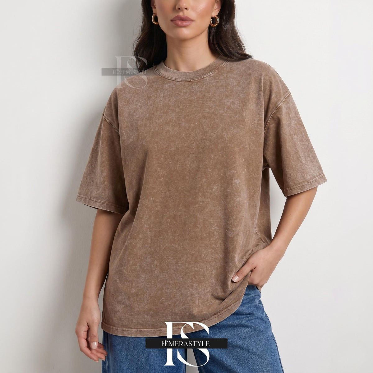 May include: A brown, oversized t-shirt with short sleeves. The shirt has a textured, faded appearance and a crew neck. The model is wearing blue jeans. The shirt is from the brand "IEMERASTYLE".