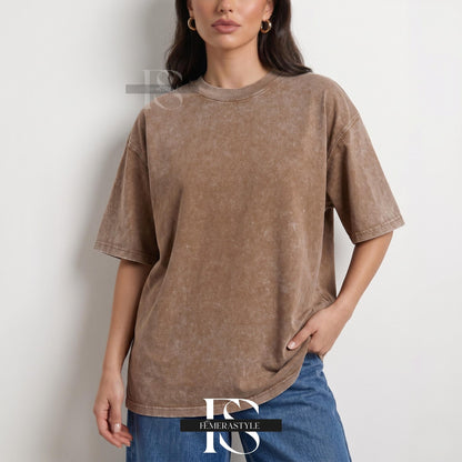 May include: A brown, oversized t-shirt with short sleeves. The shirt has a textured, faded appearance and a crew neck. The model is wearing blue jeans. The shirt is from the brand "IEMERASTYLE".