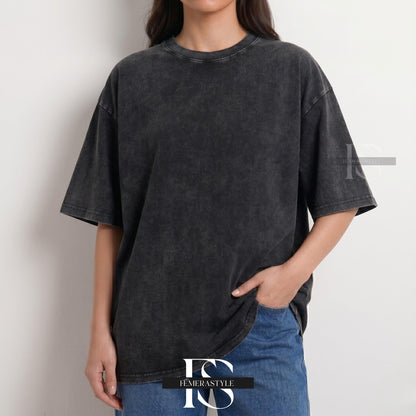 May include: A charcoal gray, oversized t-shirt with a textured, washed appearance. The short-sleeved shirt has a crew neck and a relaxed fit. The model is wearing blue jeans. The shirt is from the brand "IEMERASTYLE".