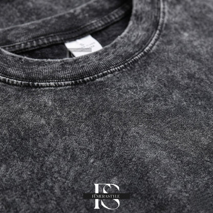 May include: Close-up of a charcoal gray t-shirt with a textured, acid wash effect. The crew neck and seams are visible, with a small white tag near the collar. The bottom right corner features the text "IEMERASTYLE" in a stylized font.