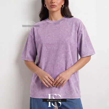 May include: A lavender-colored, short-sleeved t-shirt with a crew neck. The shirt has a slightly faded, textured appearance. The model is wearing blue jeans. The brand name "IEMERASTYLE" is visible at the bottom of the image.