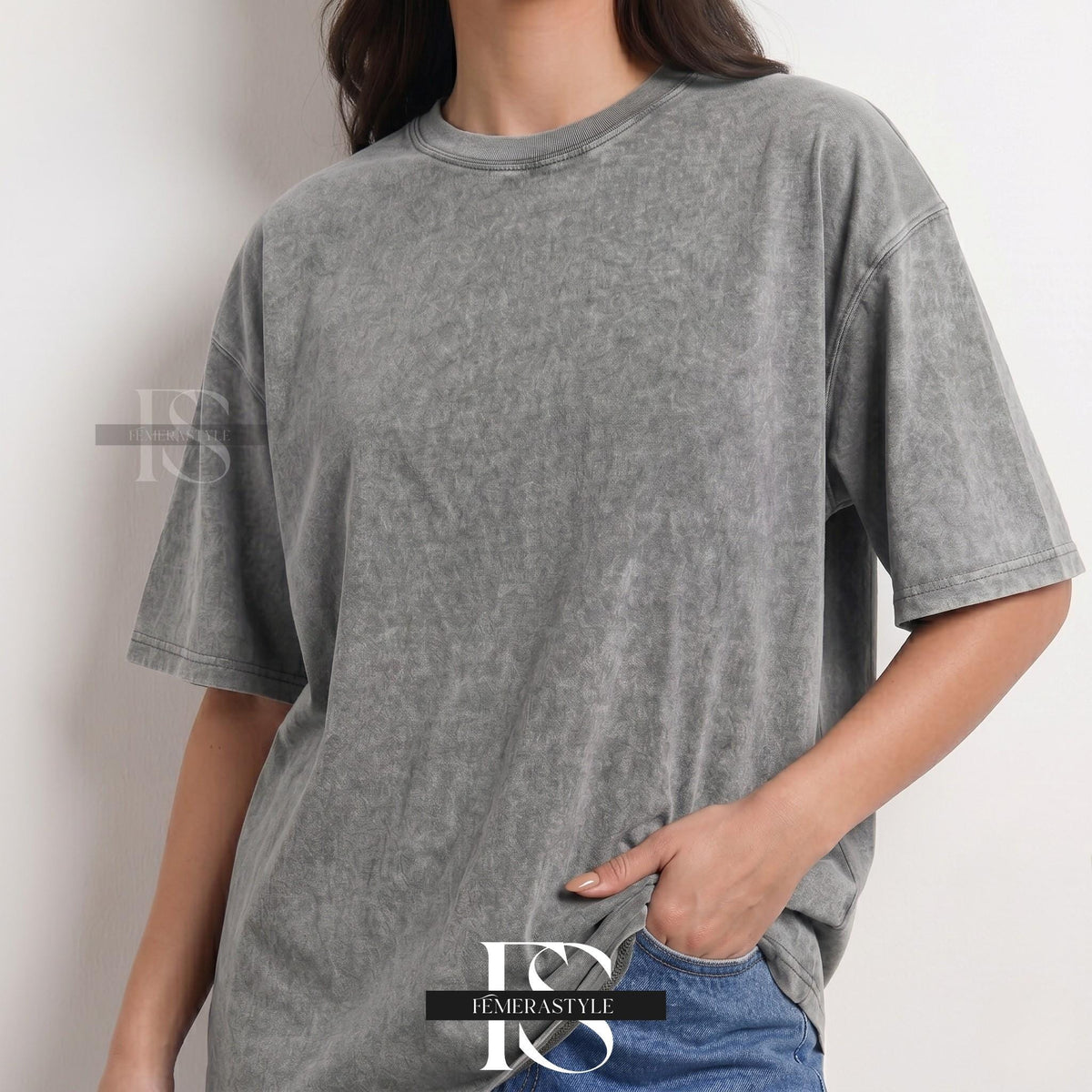 May include: A gray, acid-wash t-shirt with short sleeves. The shirt has a crew neck and a slightly oversized fit. The fabric has a textured appearance. The shirt is paired with blue jeans. The brand name "IEMERASTYLE" is visible.