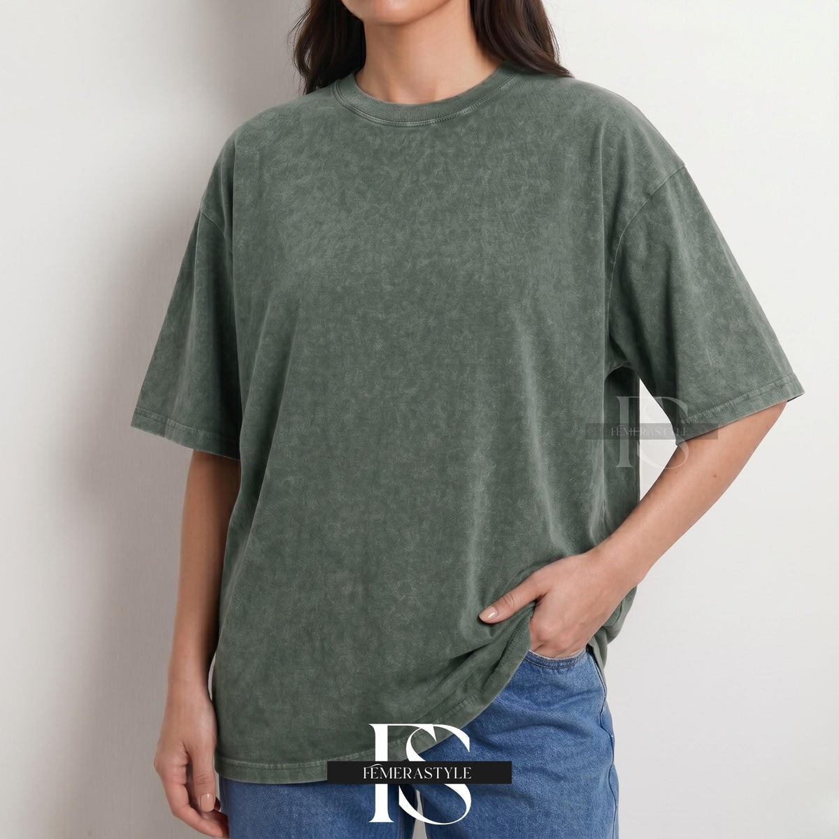 May include: A washed-out olive green t-shirt with a crew neck and short sleeves. The shirt has a slightly oversized fit and a textured appearance. The model is wearing blue jeans. The logo "IEMERASTYLE" is visible at the bottom.