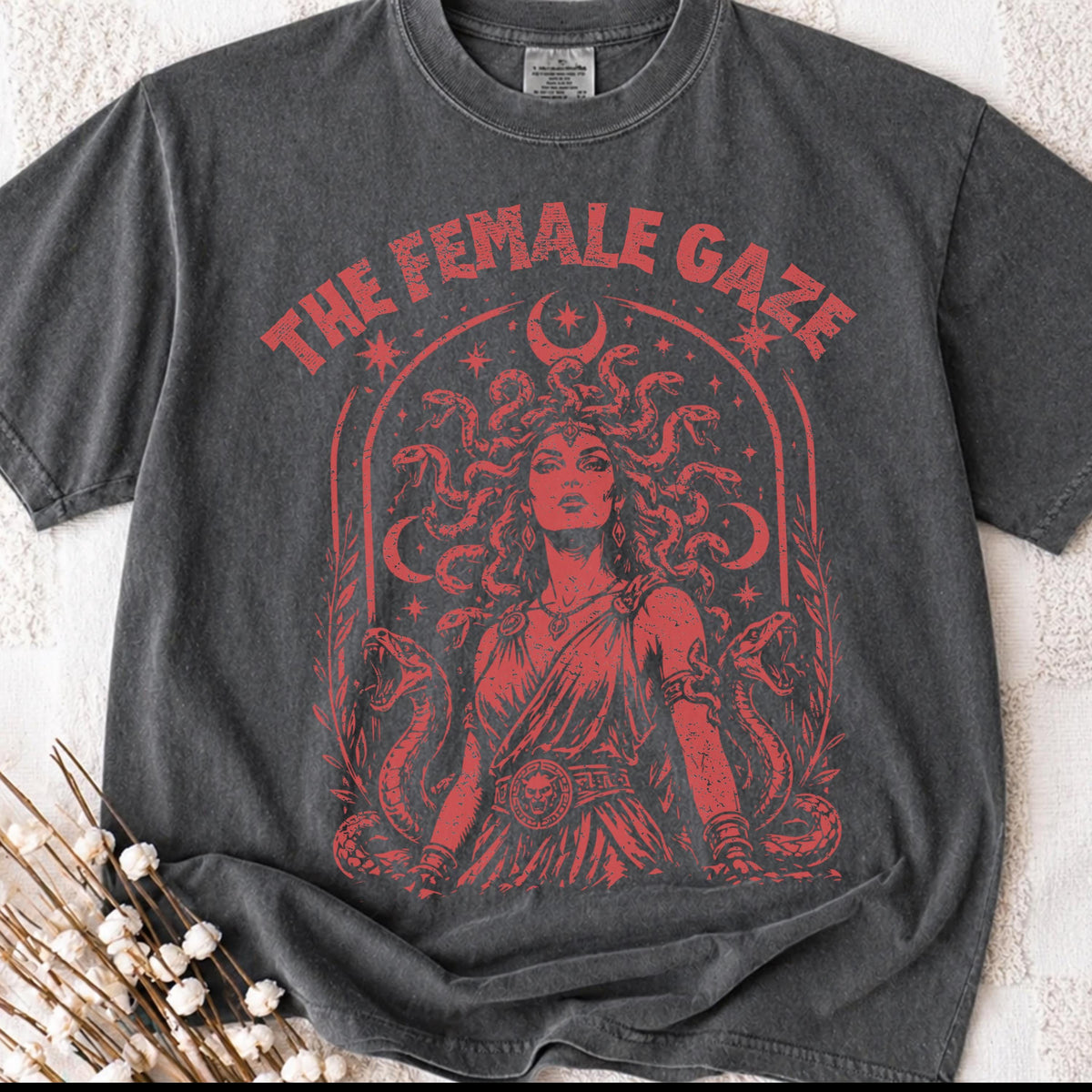 May include: Dark gray t-shirt featuring a red graphic of a woman with snakes for hair, the text "THE FEMALE GAZE", and a crescent moon. The design is vintage-inspired.