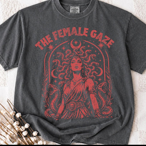 May include: Dark gray t-shirt featuring a red graphic of a woman with snakes for hair, the text "THE FEMALE GAZE", and a crescent moon. The design is vintage-inspired.