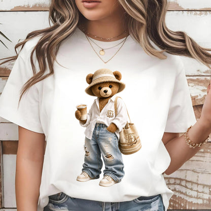 May include: White t-shirt featuring a cartoon bear wearing a straw hat, white shirt, ripped jeans, and sneakers. The bear holds a coffee cup and a beige tote bag with the letter "D". The bear is a whimsical design.