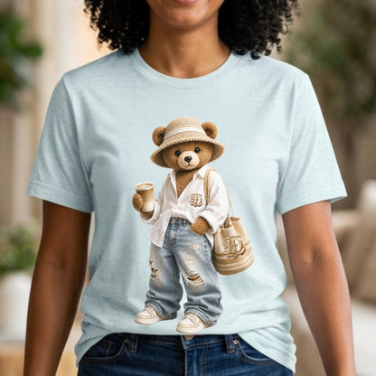 May include: Light blue t-shirt featuring a cartoon bear wearing a white shirt, ripped jeans, and a straw hat. The bear is holding a coffee cup and a tote bag with the letter "H" on it. The bear is wearing white sneakers.