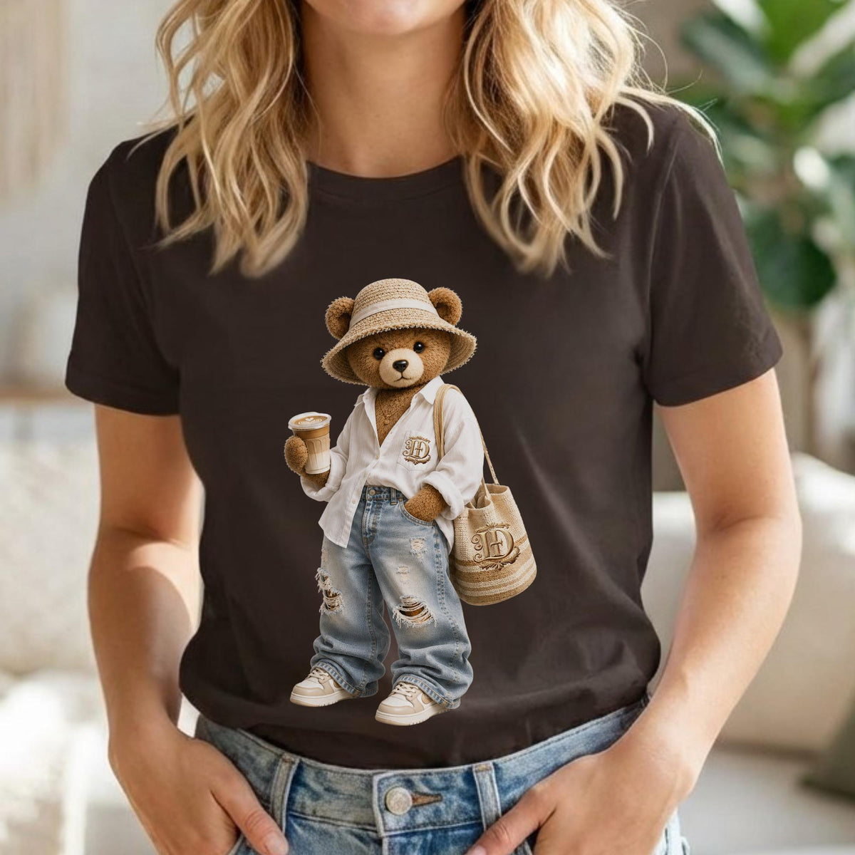 May include: Brown t-shirt featuring a cartoon bear wearing a straw hat, white shirt, ripped jeans, and sneakers. The bear is holding a coffee cup and a tote bag with the letter "H".