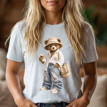May include: Light gray t-shirt featuring a cartoon bear wearing a straw hat, white shirt, ripped jeans, and sneakers. The bear holds a coffee cup and a beige tote bag with a monogram. The bear is a whimsical design.