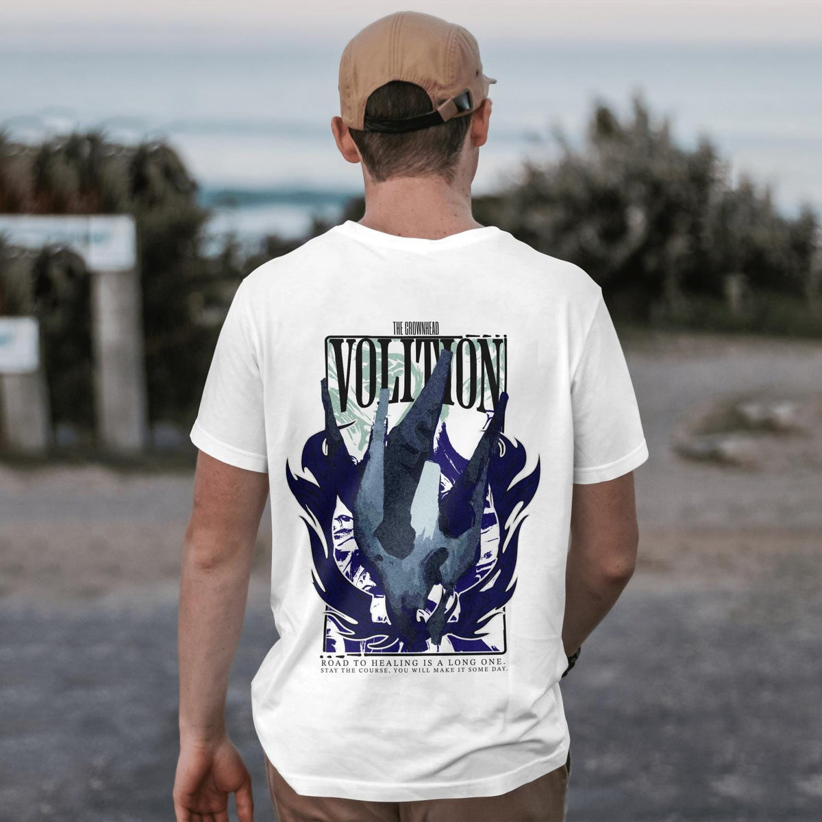 May include: A white t-shirt featuring a graphic on the back with the text "THE GROWNHEAD VOLITION" and "ROAD TO HEALING IS A LONG ONE. STAY THE COURSE, YOU WILL MAKE IT SOME DAY." The design includes a dark blue abstract shape and a rectangular frame.