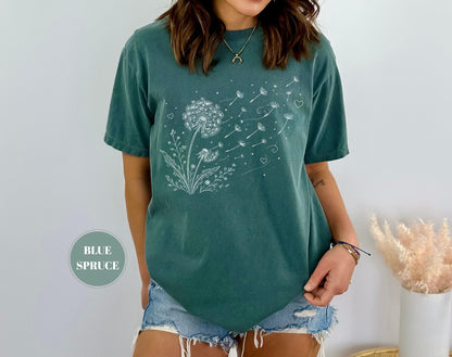 May include: Blue spruce t-shirt featuring a white dandelion design with floating seeds and hearts. The t-shirt has short sleeves and a relaxed fit. The words "BLUE SPRUCE" are printed on a circular label.