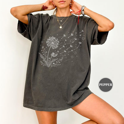 May include: Dark gray t-shirt featuring a white dandelion design with seeds blowing away. The graphic includes hearts and small dots. The shirt has short sleeves and a relaxed fit. The word "PEPPER" is in a circle on the bottom right.