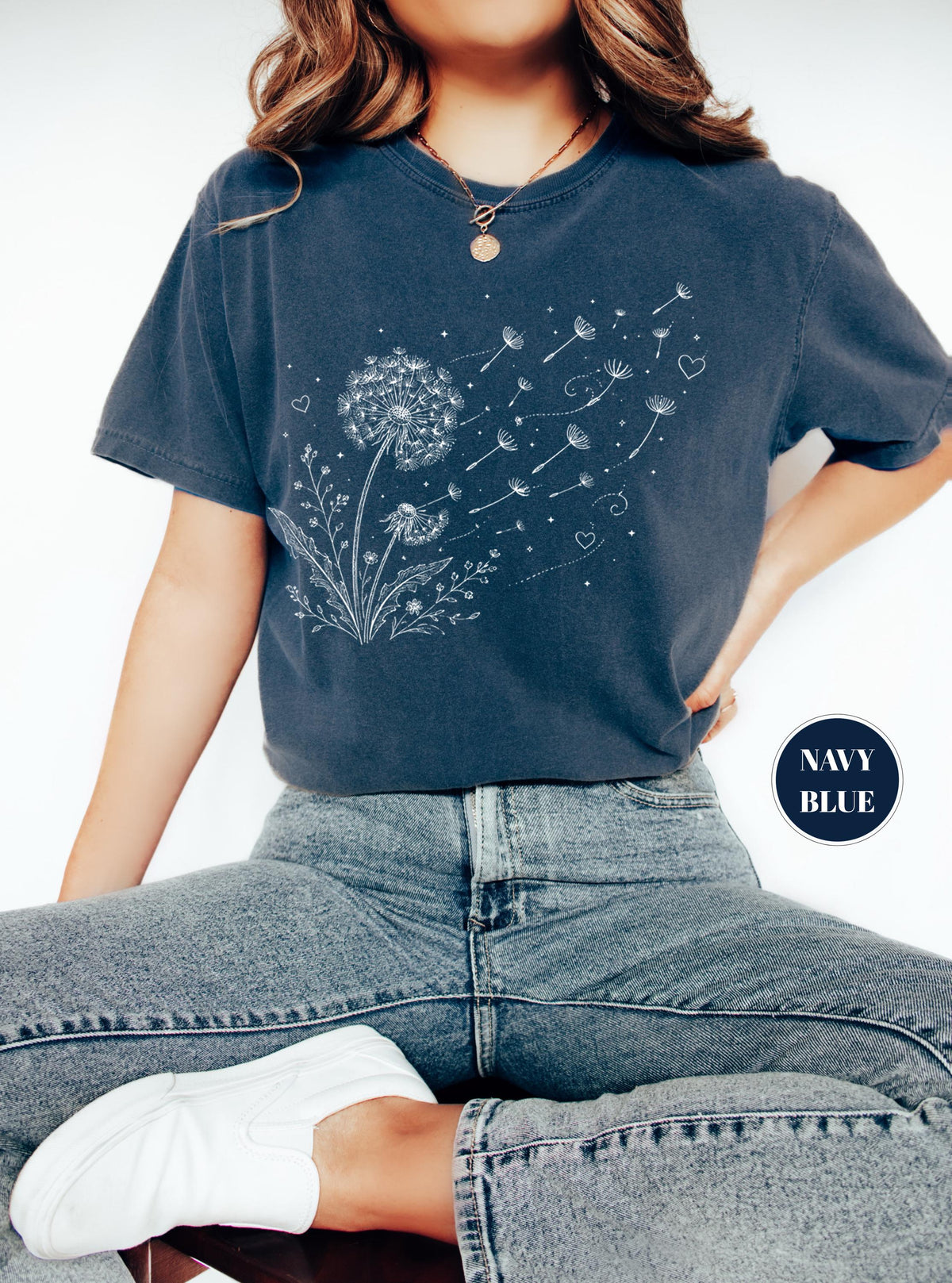 May include: Navy blue t-shirt featuring a white dandelion design with floating seeds and hearts. The shirt has short sleeves and a relaxed fit. The words "NAVY BLUE" are in a navy blue circle in the lower right corner.