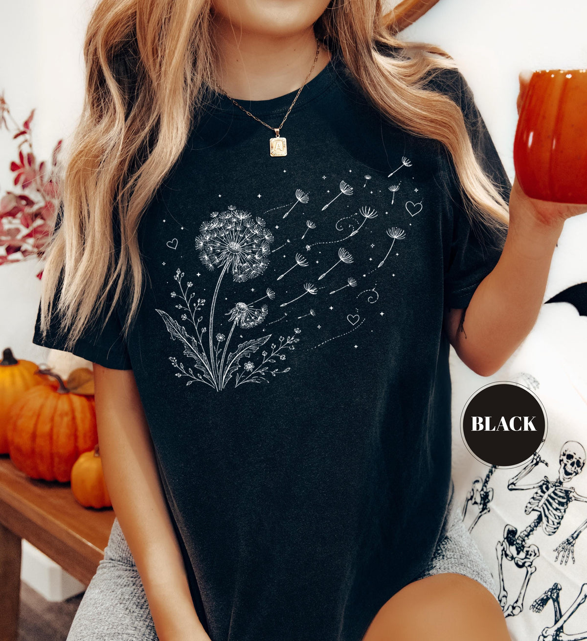 May include: Black t-shirt featuring a white dandelion design with seeds blowing away. The graphic includes hearts and dots. The shirt has short sleeves and a round neckline. A black circle with the word "BLACK" is on the shirt.
