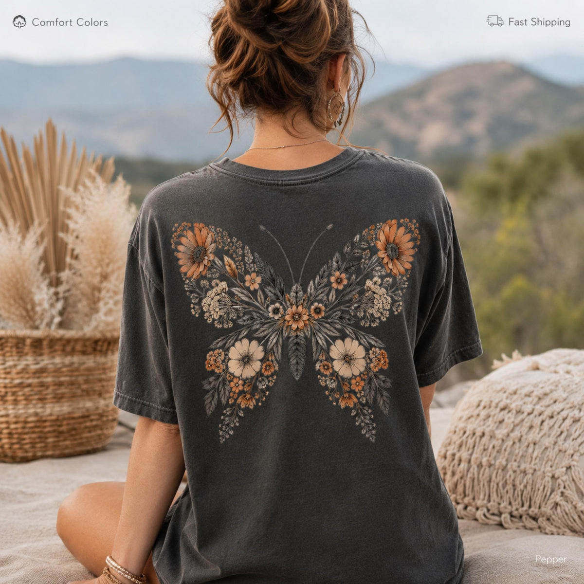 May include: A charcoal gray short-sleeve t-shirt featuring a large graphic on the back. The graphic depicts a butterfly shape composed of various orange, cream, and brown flowers, leaves, and stems. The shirt has a crew neckline and a relaxed fit.