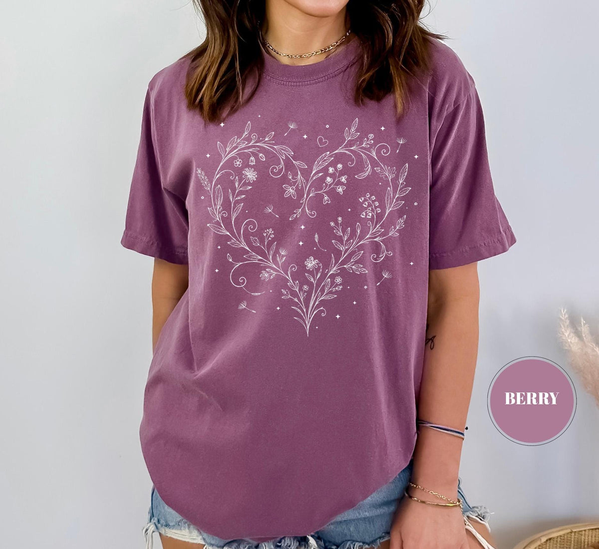 May include: Berry-colored t-shirt with a white floral heart design. The design features delicate flowers, leaves, and small details. The shirt has short sleeves and a relaxed fit, perfect for casual wear.