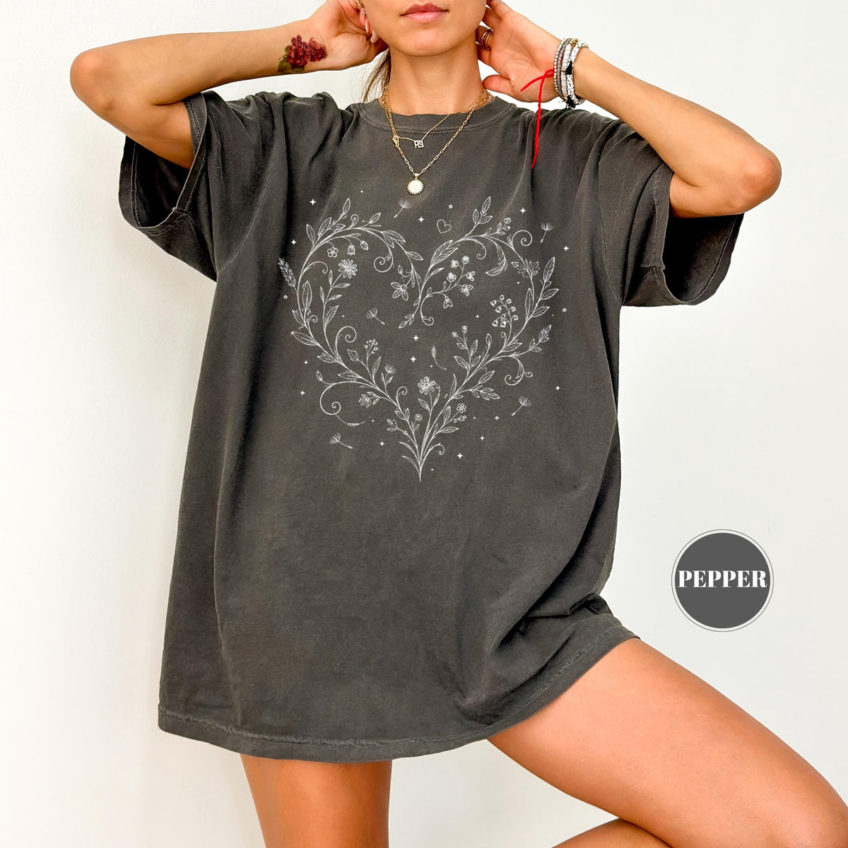 May include: Dark gray t-shirt featuring a white floral heart design. The design includes delicate flowers, leaves, and small details. The shirt has short sleeves and a relaxed fit. The word "PEPPER" is printed on the bottom right.