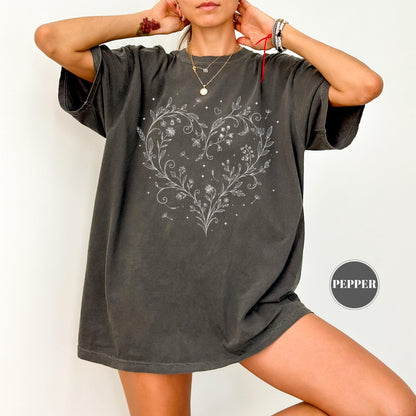 May include: Dark gray t-shirt featuring a white floral heart design. The design includes delicate flowers, leaves, and small details. The shirt has short sleeves and a relaxed fit. The word "PEPPER" is printed on the bottom right.