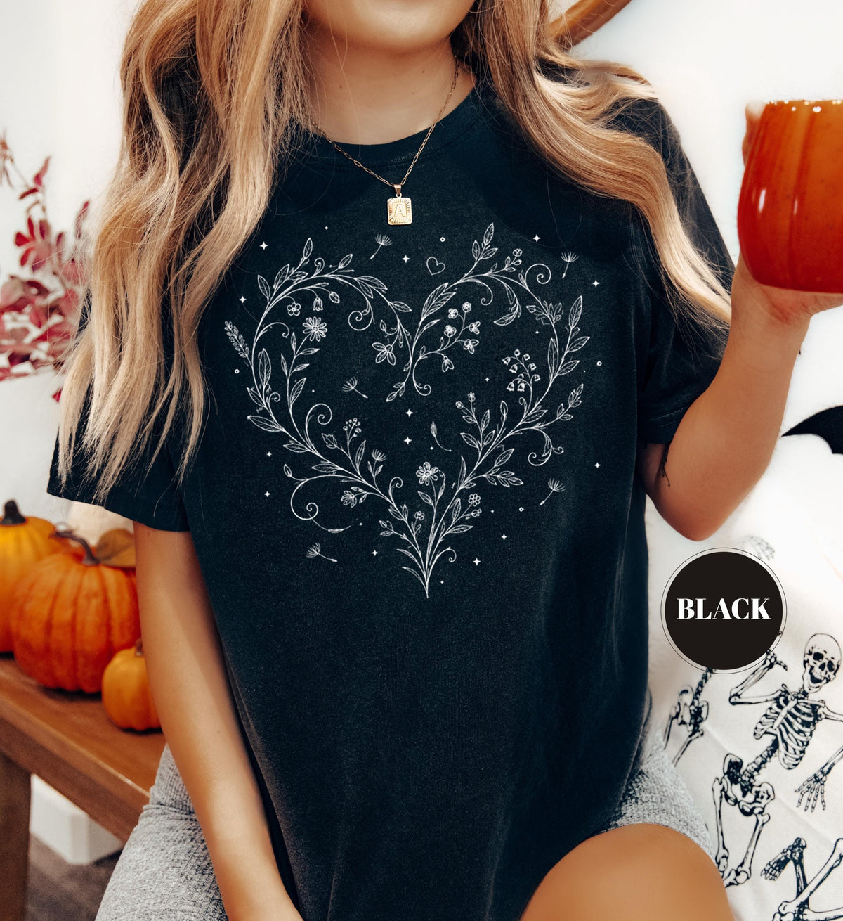 May include: Black t-shirt featuring a white floral heart design. The heart is composed of delicate leaves, flowers, and small stars. The shirt has short sleeves and a round neckline. A black circle with the word "BLACK" is on the bottom right.