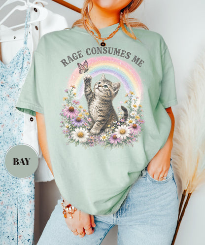May include: Sage green t-shirt featuring a kitten reaching for a butterfly in front of a rainbow and flowers. The text "RAGE CONSUMES ME" is arched above the design. The shirt is a relaxed fit.