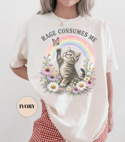 May include: Ivory-colored t-shirt featuring a graphic of a kitten reaching for a butterfly above a rainbow and flowers. The text "RAGE CONSUMES ME" is arched above the design. The shirt has short sleeves.