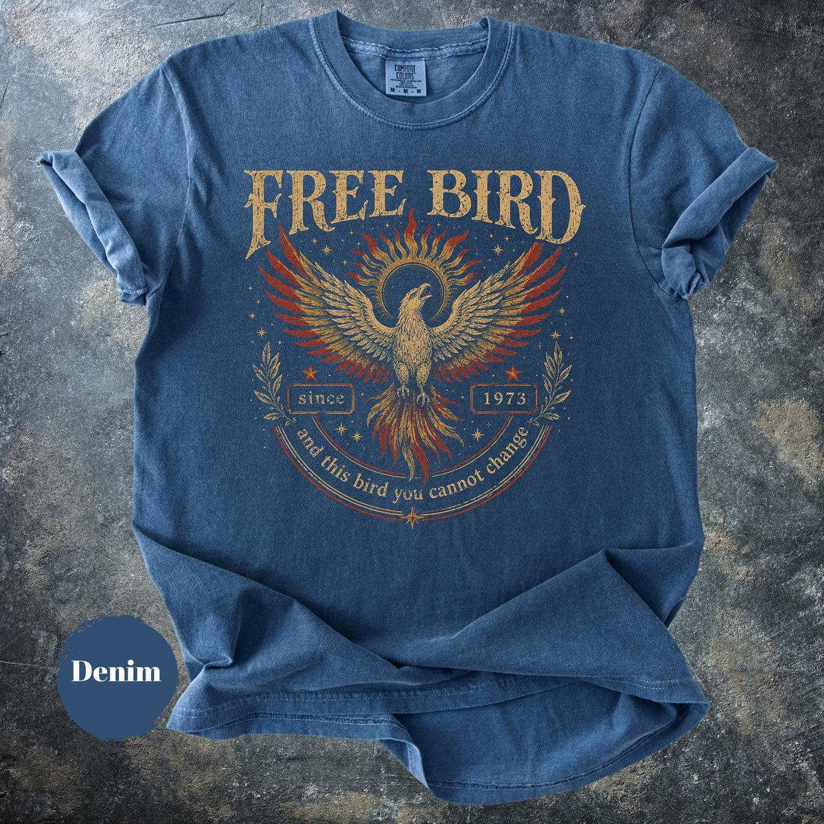 May include: Denim blue t-shirt with a distressed graphic of a phoenix and the words "FREE BIRD" above it. The graphic includes the text "since 1973" and "and this bird you cannot change".