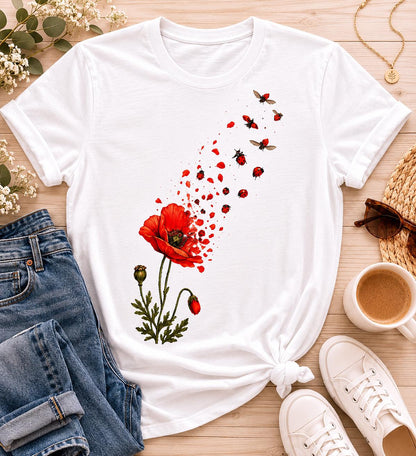 May include: A white short-sleeved t-shirt featuring a graphic print of a red poppy flower with green stems and leaves. The flower petals appear to be disintegrating into a swarm of small red ladybugs that drift upward across the fabric surface.
