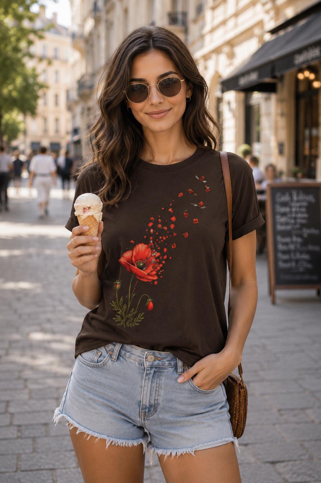 May include: A dark brown short-sleeved t-shirt featuring a graphic print of a vibrant red poppy flower with petals appearing to drift upward and away. The shirt has a crew neckline and rolled sleeves, paired with light blue denim shorts.