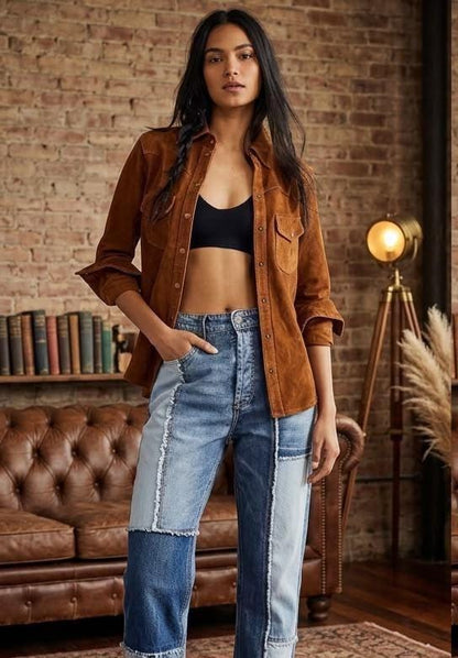 May include: A brown suede button-down shirt with long sleeves and two chest pockets, worn over a black crop top, paired with high-waisted blue jeans featuring a multi-tonal patchwork design with frayed seams and a straight-leg silhouette.