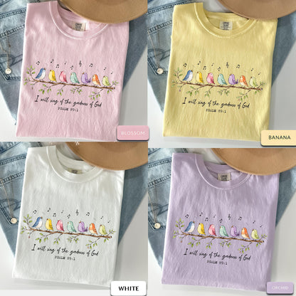 May include: Four short-sleeve t-shirts in blossom pink, banana yellow, white, and orchid purple. Each shirt features a graphic of seven colorful birds perched on a branch with musical notes and the text I will sing of the goodness of God PSALM 89:1.
