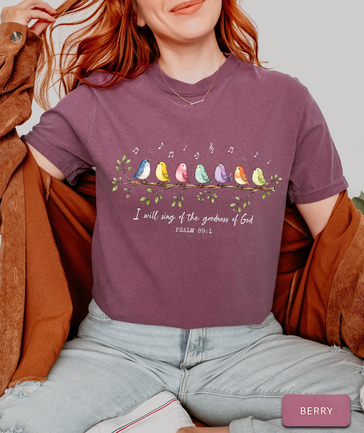 May include: A berry-colored short-sleeve t-shirt featuring a graphic of eight colorful birds perched on a leafy branch with musical notes above them. The text reads, "I will sing of the goodness of God" followed by "PSALM 89:1" in white lettering.