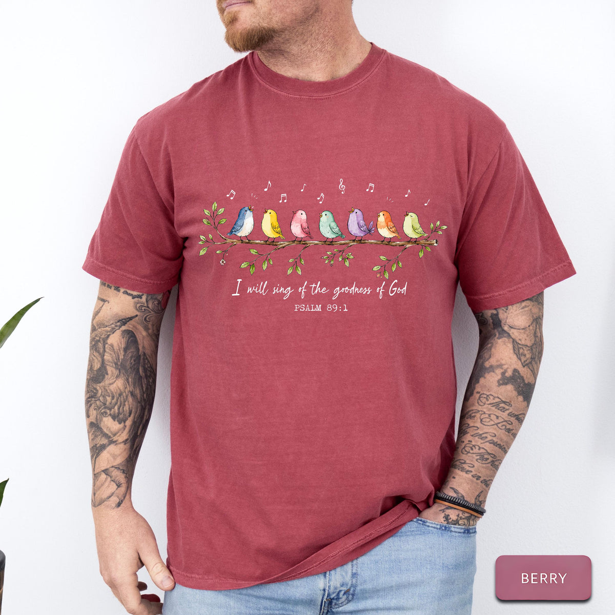 May include: A berry-colored short-sleeve t-shirt featuring a graphic of seven colorful birds perched on a leafy branch with musical notes above them. Below the birds, the text reads, I will sing of the goodness of God, PSALM 89:1.