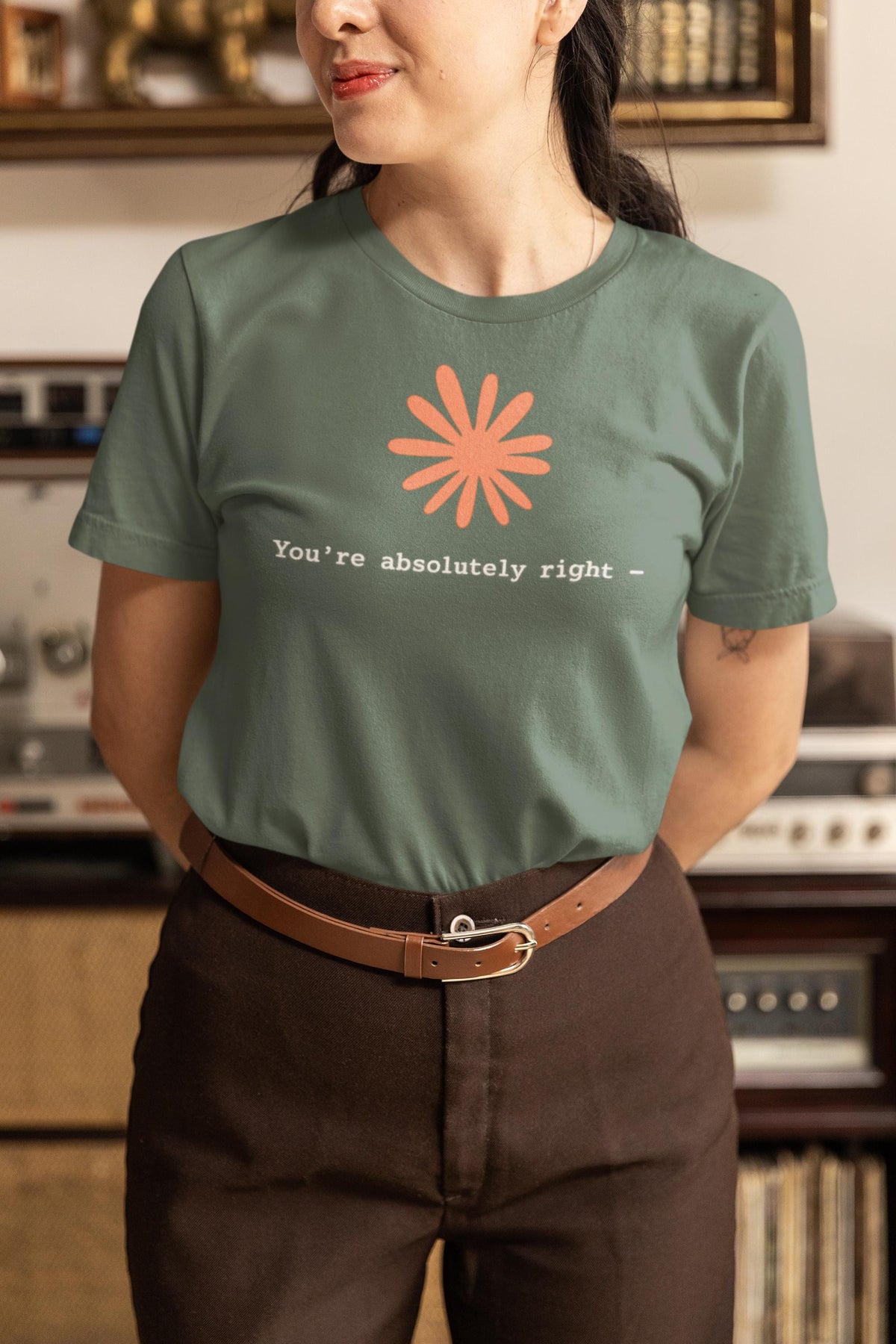 May include: A sage green short-sleeved t-shirt featuring a coral-colored flower graphic centered above the white text that reads, "You're absolutely right -" in a simple, clean font. The shirt has a crew neckline and a standard fit.
