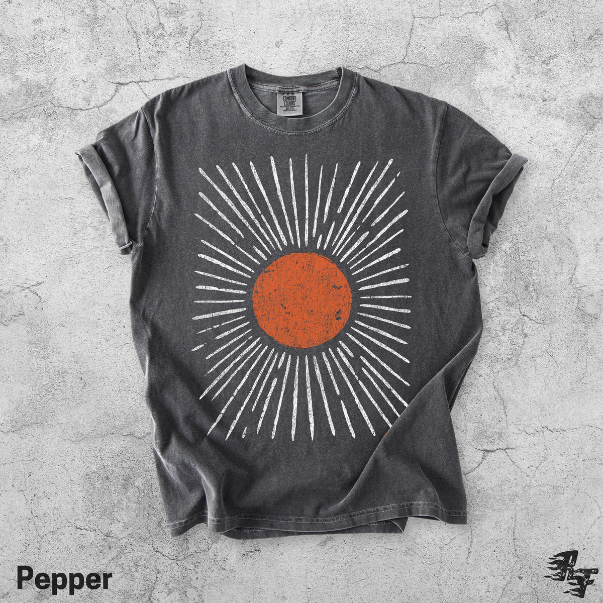 May include: A charcoal grey short-sleeve t-shirt featuring a central graphic of a distressed orange circle surrounded by radiating white lines. The shirt has a crew neckline and a vintage-style wash, with a small tag visible at the inner collar.