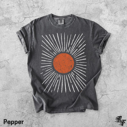 May include: A charcoal grey short-sleeve t-shirt featuring a central graphic of a distressed orange circle surrounded by radiating white lines. The shirt has a crew neckline and a vintage-style wash, with a small tag visible at the inner collar.