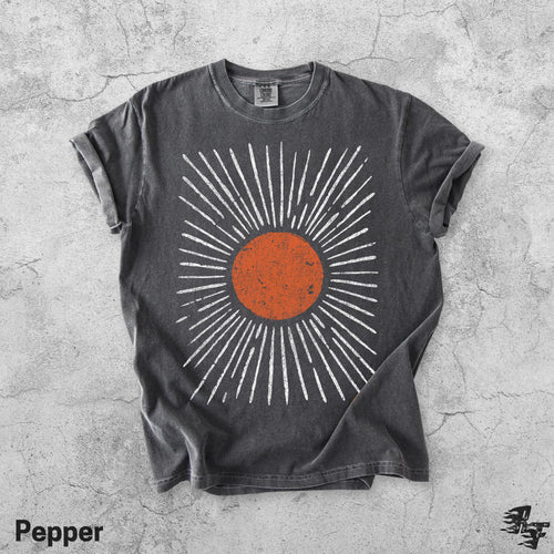 May include: A charcoal grey short-sleeve t-shirt featuring a central graphic of a distressed orange circle surrounded by radiating white lines. The shirt has a crew neckline and a vintage-style wash, with a small tag visible at the inner collar.