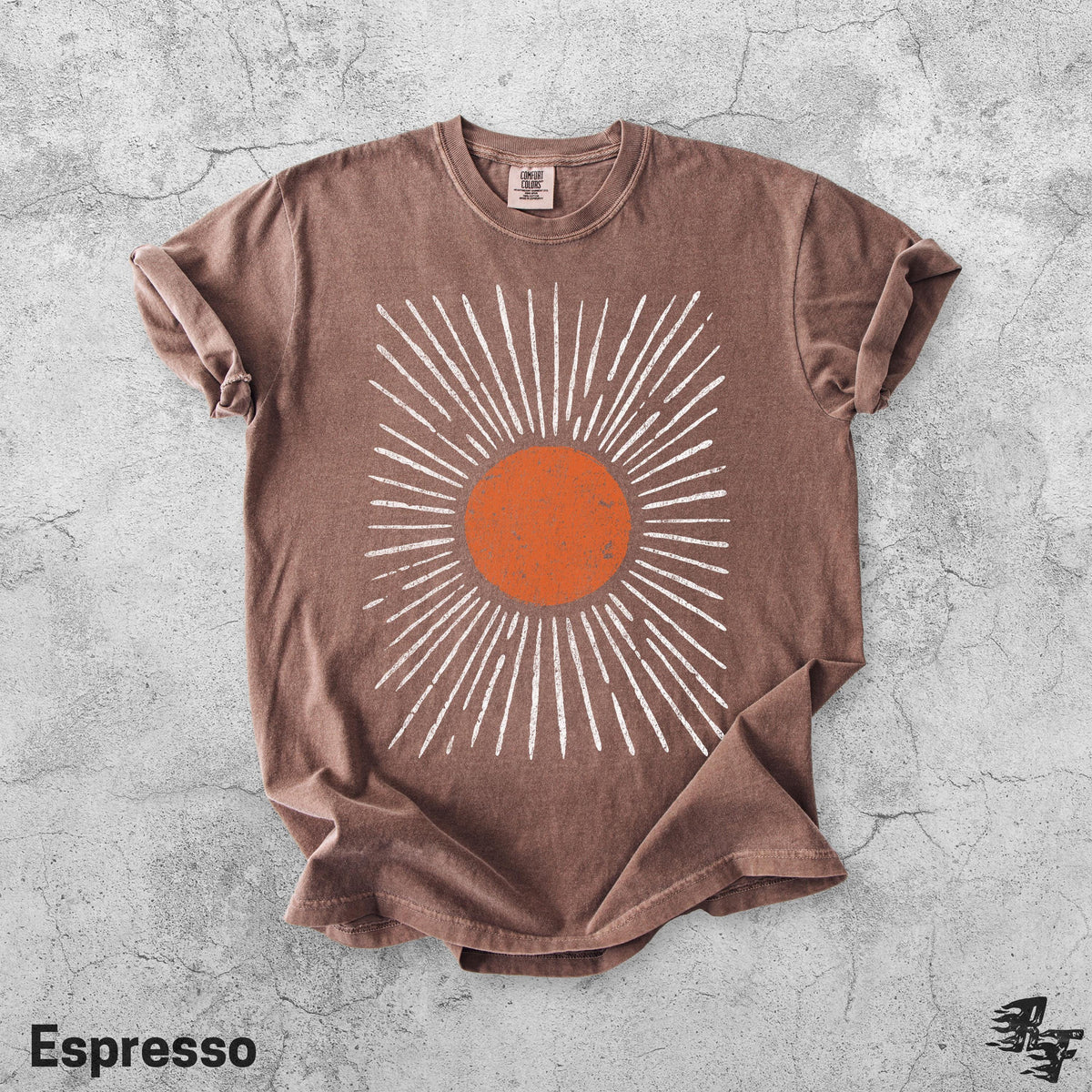 May include: A brown short-sleeve t-shirt featuring a central graphic of a solid orange circle surrounded by radiating white lines. The shirt has a crew neckline and a tag at the inner collar. The fabric has a slightly faded, worn-in appearance.