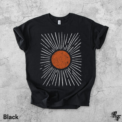 May include: A black short-sleeve t-shirt featuring a central graphic of a distressed orange circle surrounded by radiating white lines. The design has a textured, weathered appearance, and the shirt has a standard crew neckline and short sleeves.