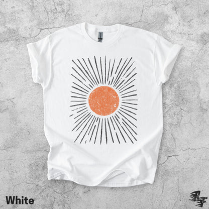 May include: A white short-sleeved t-shirt featuring a central graphic of a distressed orange circle surrounded by radiating black lines. The design has a textured, weathered appearance. The shirt has a crew neckline and a standard fit.