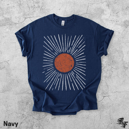 May include: A navy blue short-sleeve t-shirt featuring a central graphic of a distressed, textured orange circle surrounded by radiating white lines that extend outward in a sunburst pattern. The shirt has a crew neckline and a standard fit.