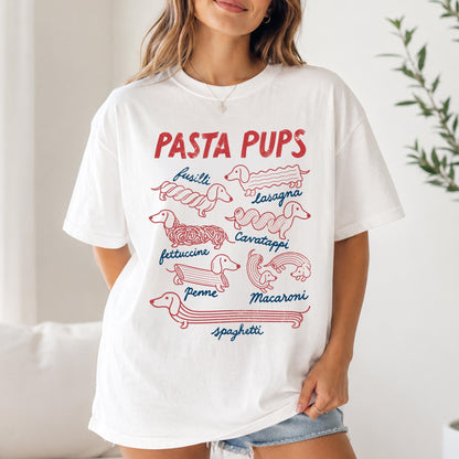 May include: A white short-sleeve t-shirt featuring a red graphic with the text PASTA PUPS and illustrations of dachshunds shaped like various pasta types, including fusilli, lasagna, cavatappi, fettuccine, penne, macaroni, and spaghetti in blue text.
