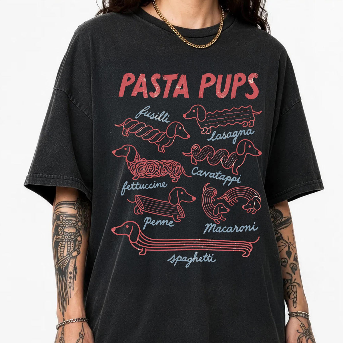 May include: A charcoal black short-sleeve t-shirt featuring a graphic print titled PASTA PUPS in red text. The design displays various dachshund dogs illustrated as different pasta shapes, labeled with the words fusilli, lasagna, cavatappi, fettuccine, penne, macaroni, and spaghetti.